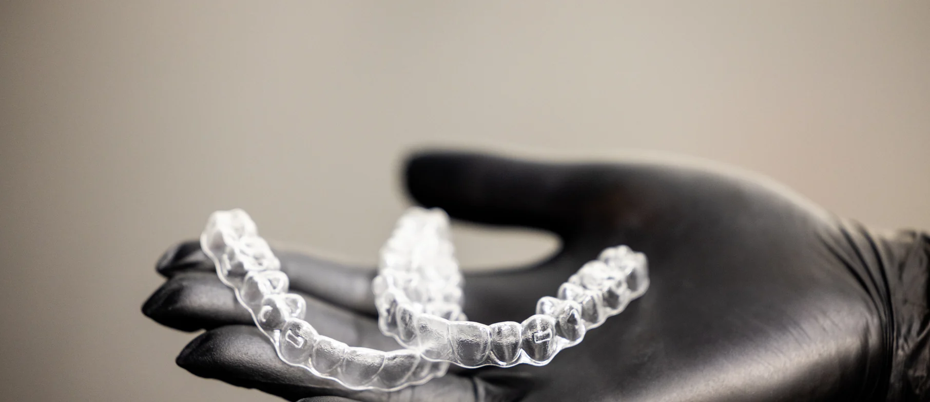 A clear aligner tray held in a gloved hand